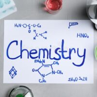 laboratory-glassware-paper-word-chemistry-grey-background-flat-lay-142768247